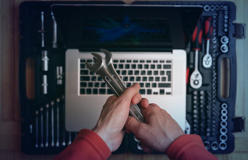 Hands holding two wrenches above a laptop, representing software tools